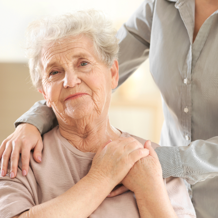 Older adult holding a caregiver’s hand while receiving comfort and support at home.