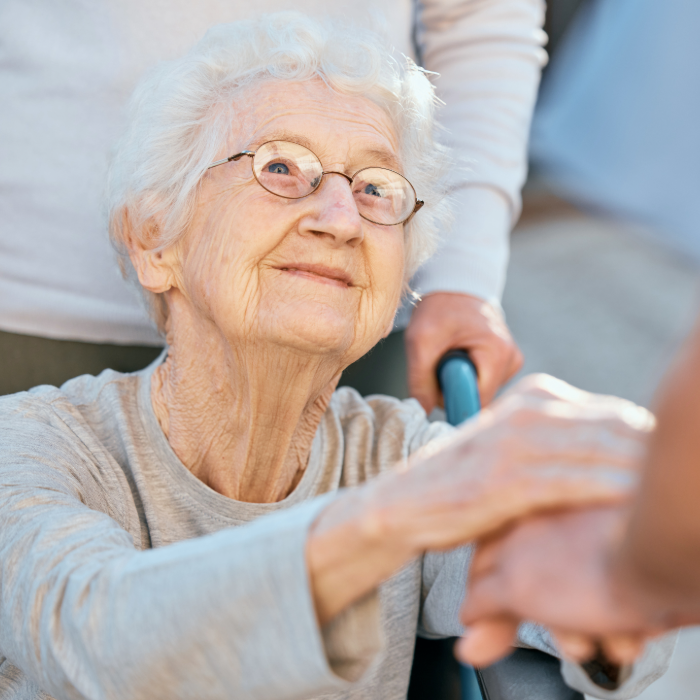 Older adult reaching out while being assisted by a caregiver.
